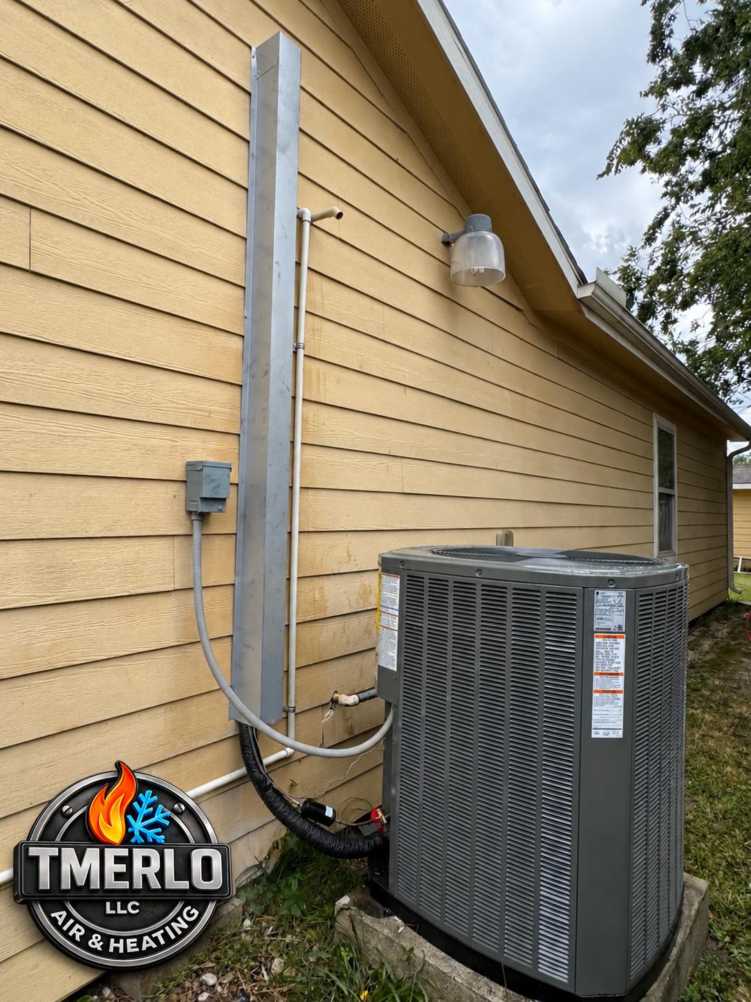 Outdoor condenser beside yellow siding with protected refrigerant lines and TMerlo logo